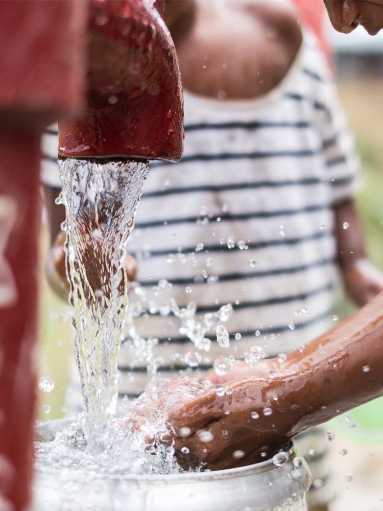 Hands being washed in fresh water from a pump.