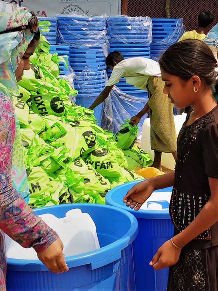 A woman and girl hold a bucket of containers.