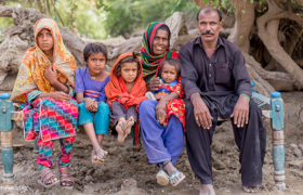A family sit with their children against a backdrop of trees.