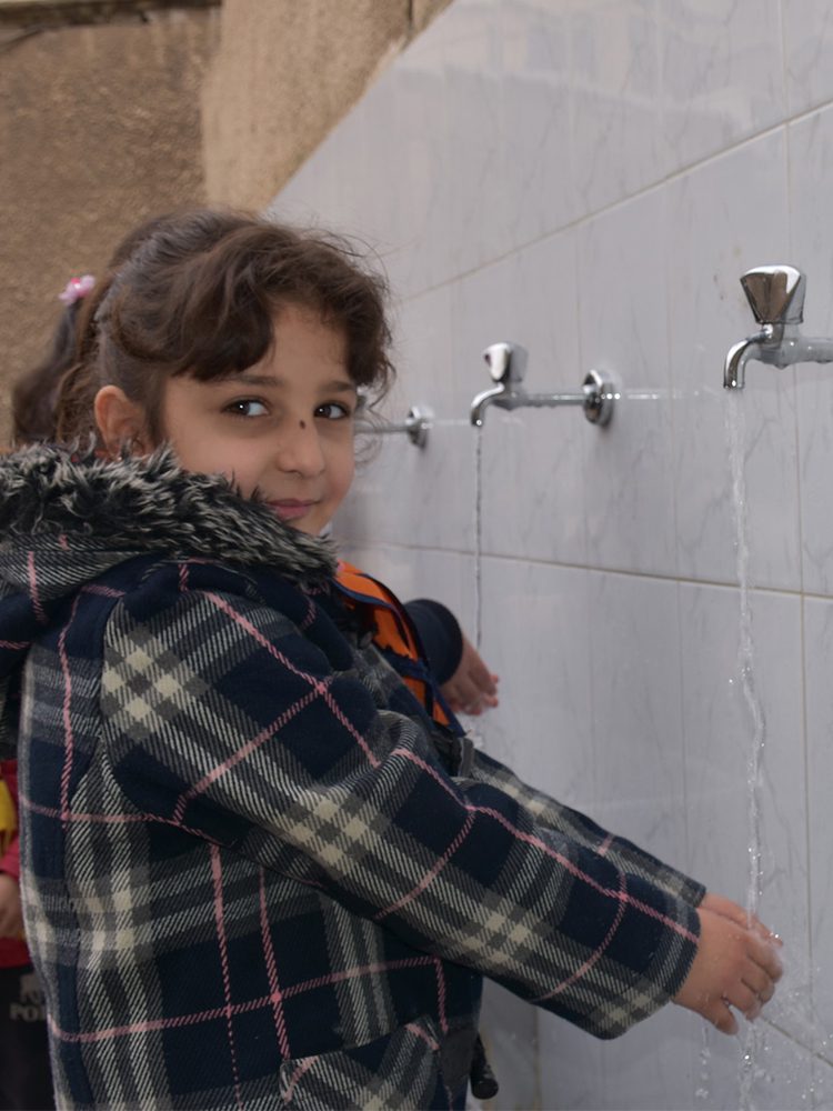 A young girl washes her hands at a basin.