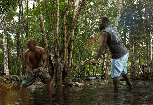 Two men shift buckets of water from a flooded stream.