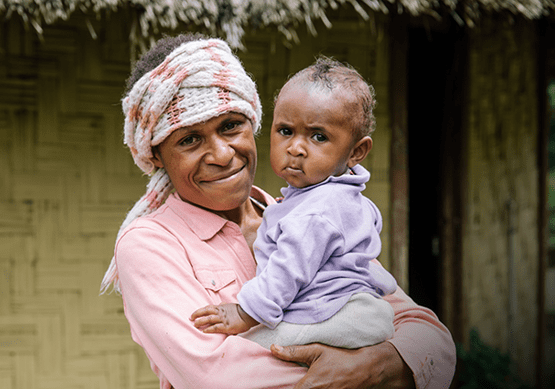 A women holds her young child outside a brown building.