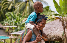 A mother carries her young child on her shoulder.