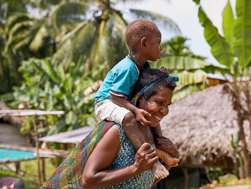 A mother carries her young child on her shoulder.