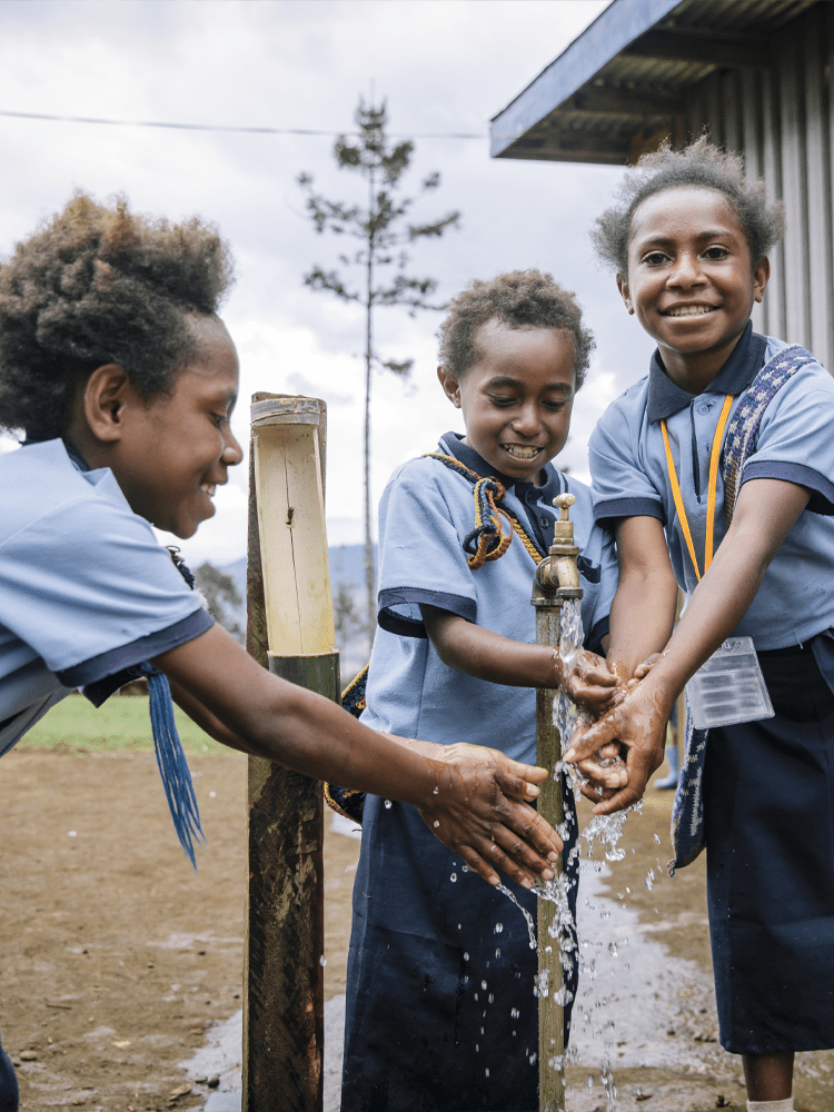 Three school children wash their hands with water from a tap