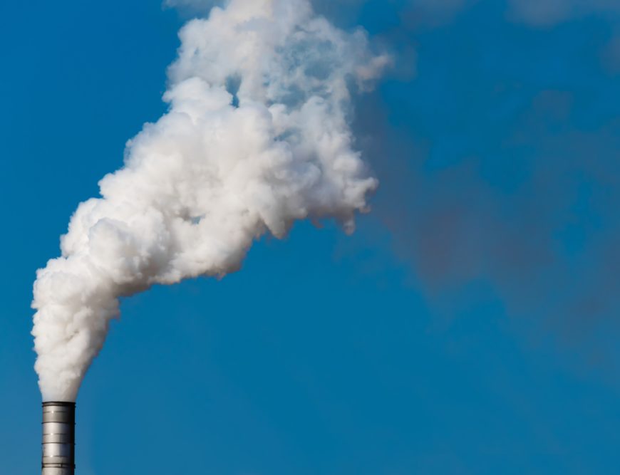 White smoke pours out of a chimney against a blue sky