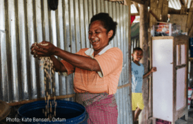 A woman wearing an orange shirt cooks over a pot
