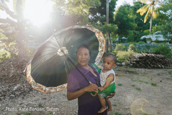 A woman shields her young child from the sun with an umbrella
