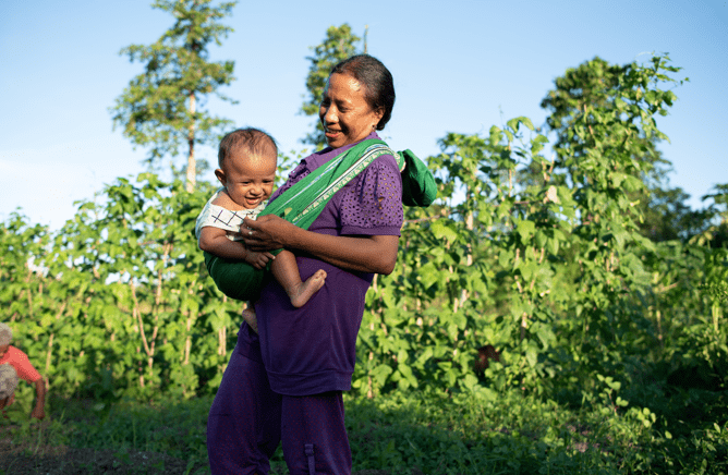 A woman holds her young baby against a green leafy background