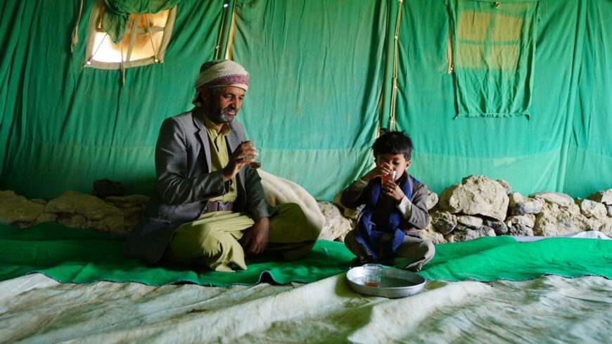 A father sits with his young son against a green background