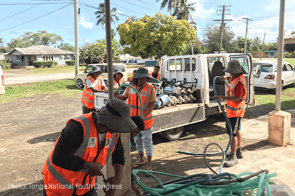 TNYC deploy water desalination units in Tonga, wearing orange rests