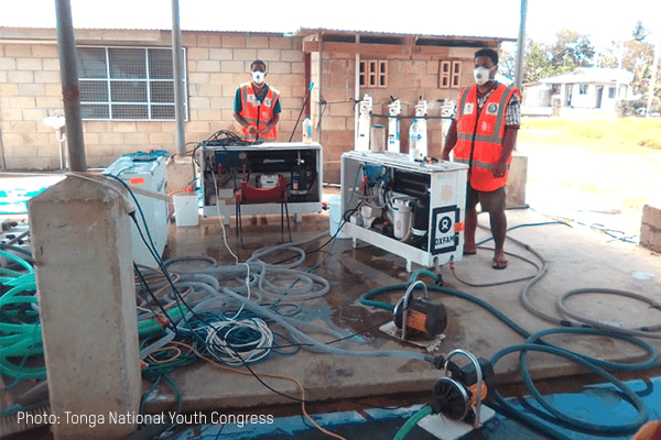 TNYC deploy water desalination units in Tonga, wearing orange rests