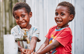Two boys wash their hands while smiling