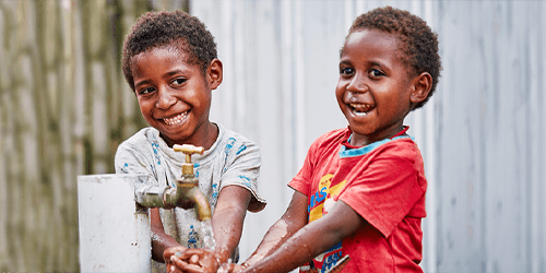 Two boys wash their hands while smiling