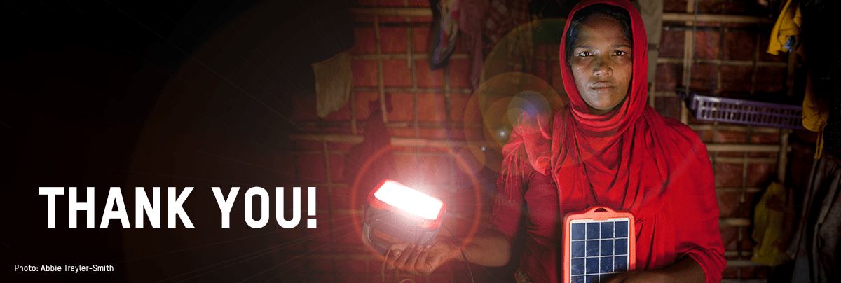 A woman wearing red holds a solar-powered light with thank you banner