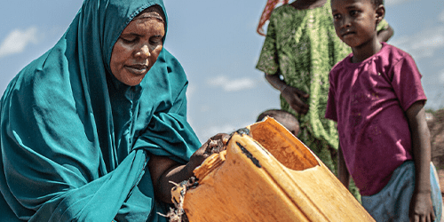 A woman collects water in a yellow container