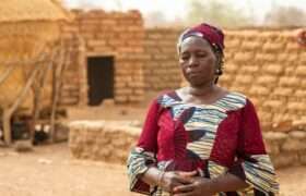 Sanfo stands outside her home