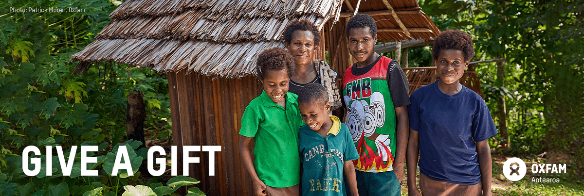 A family stand smiling in front of a bathroom structure with text 'give a gift'