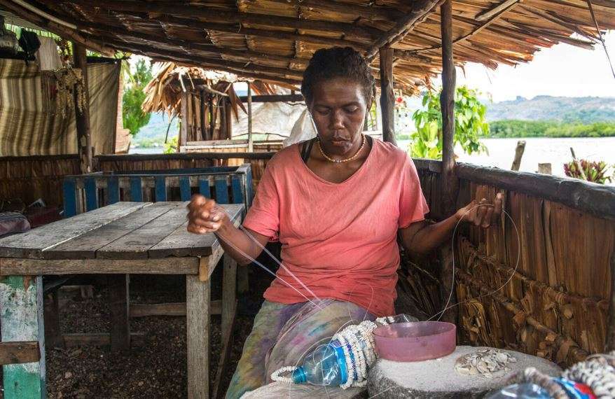 A woman wearing a pink shirt works on shell money